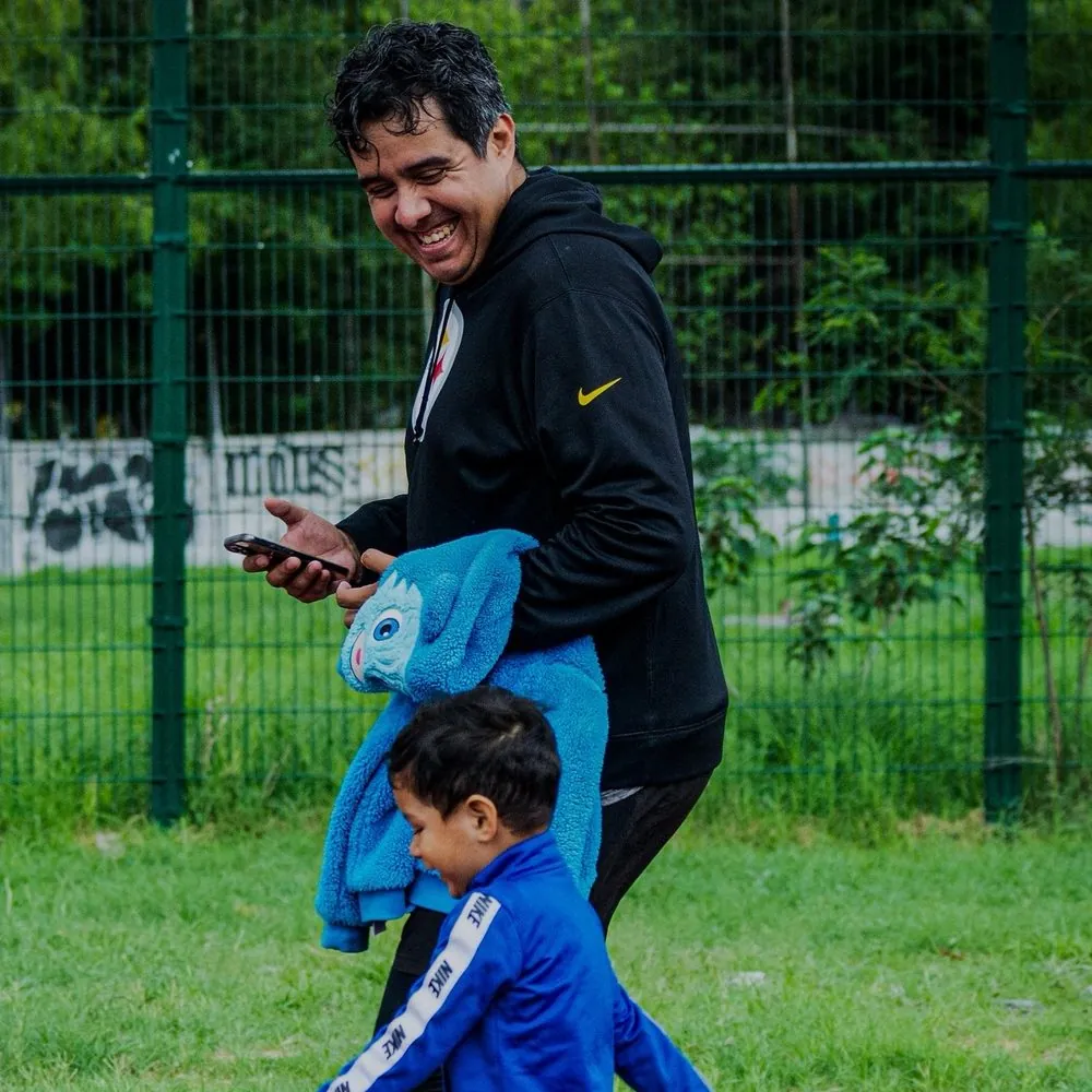 Papá riendo mientras camina en una pista de atletismo junto a su hijo pequeño